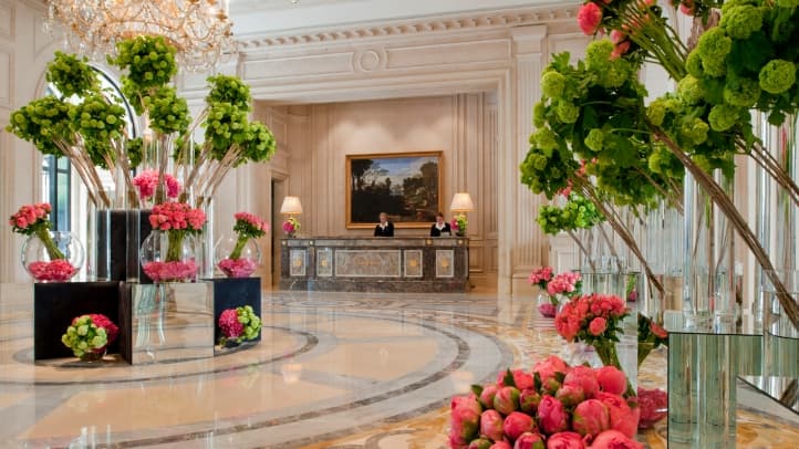 Lobby de palace parisien : marbre, lustre et immenses compositions florales devant la réception