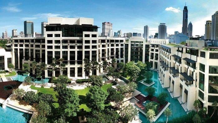 Aerial view of a Kempinski hotel complex: pools, tropical gardens and city towers beyond