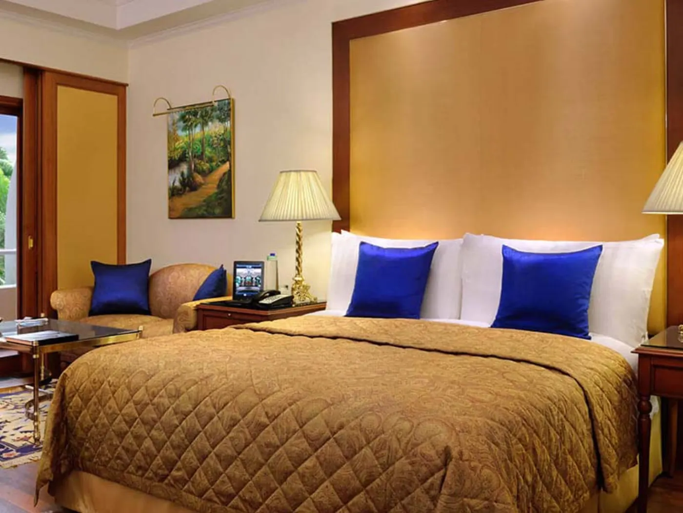 Chambre Oberoi : couvre-lit matelassé doré, coussins bleu roi et tête de lit en panneau doré