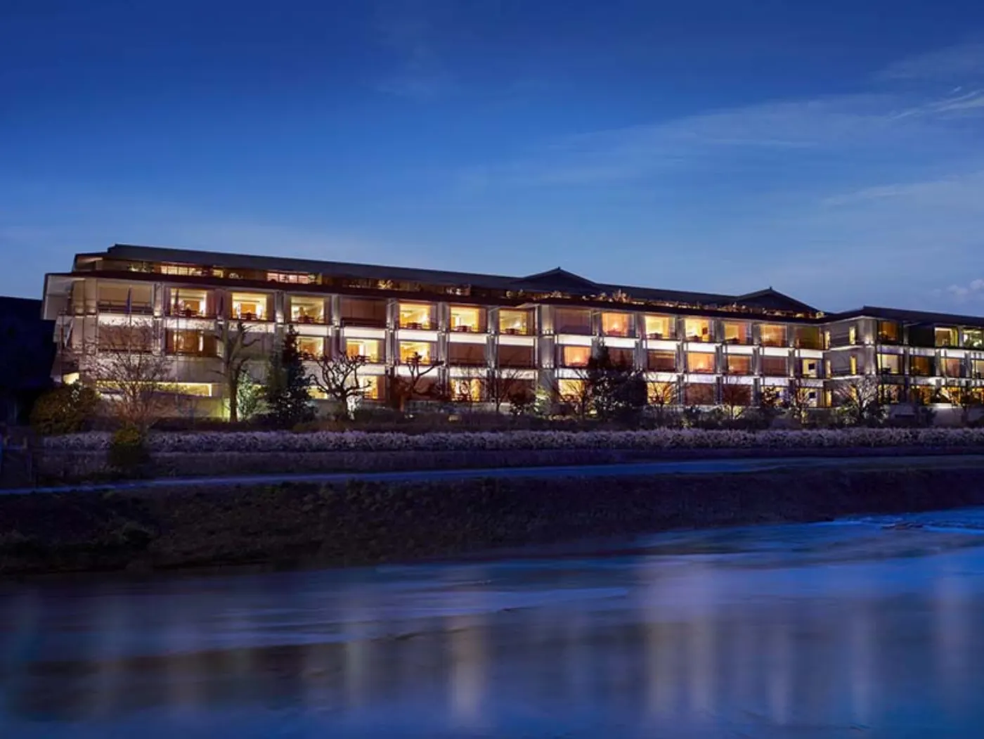 Le Ritz-Carlton Kyoto illuminé au crépuscule, ses terrasses vitrées le long de la rivière Kamo