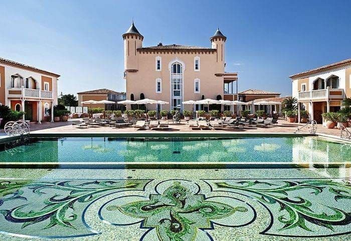 Château de la Messardière : la façade à tourelles et la piscine à mosaïque verte bordée de transats