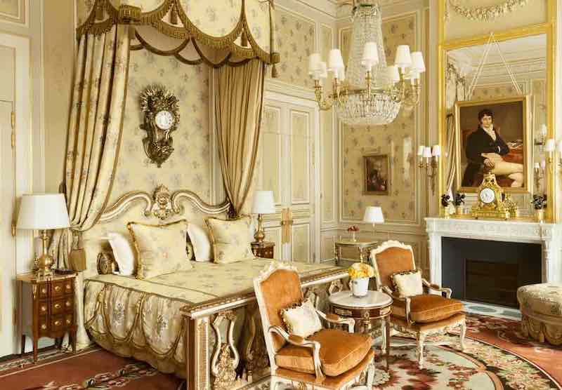 Suite de palace à la française : lit à baldaquin, lustre en cristal, cheminée de marbre et fauteuils de velours