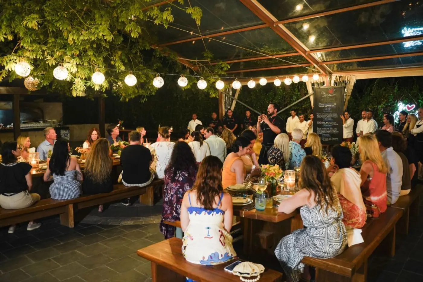 Dîner en plein air sous les guirlandes lumineuses, le chef s'adressant aux convives attablés
