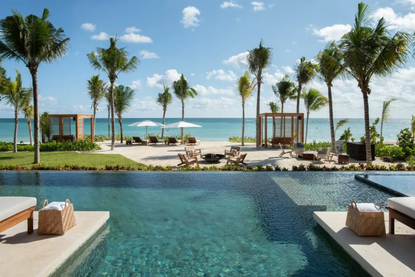 Piscine face à la mer des Caraïbes, cabanas de bois et transats sous les cocotiers