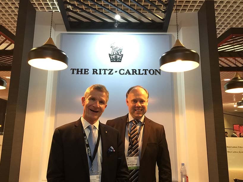 Rencontre sur le stand The Ritz-Carlton au salon ILTM de Cannes, devant le logo de la marque