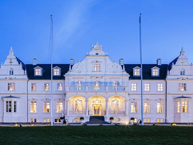 Palais hôtelier de style néoclassique illuminé au crépuscule, sa façade blanche ouverte sur la pelouse