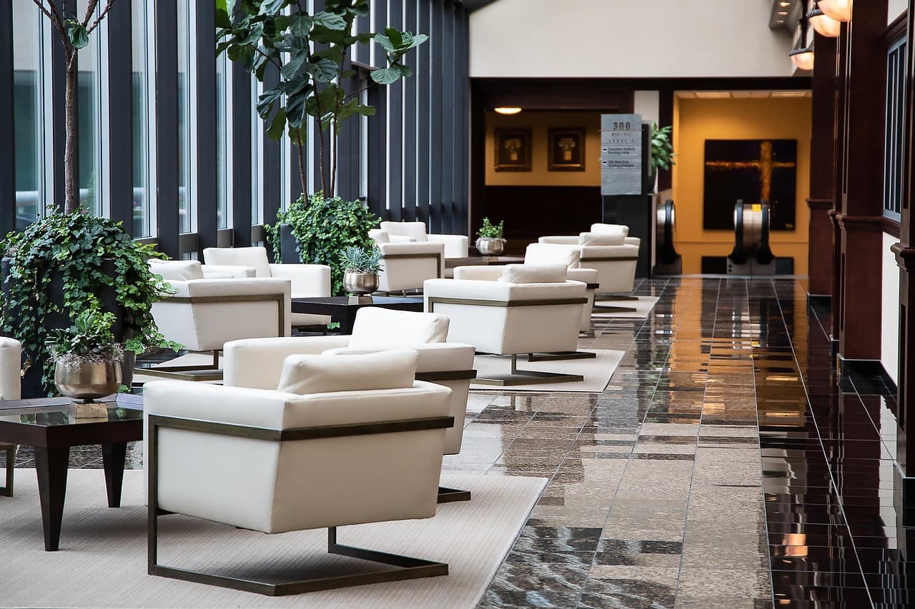Lobby d'hôtel contemporain désert : fauteuils blancs alignés, plantes vertes et sol de marbre poli