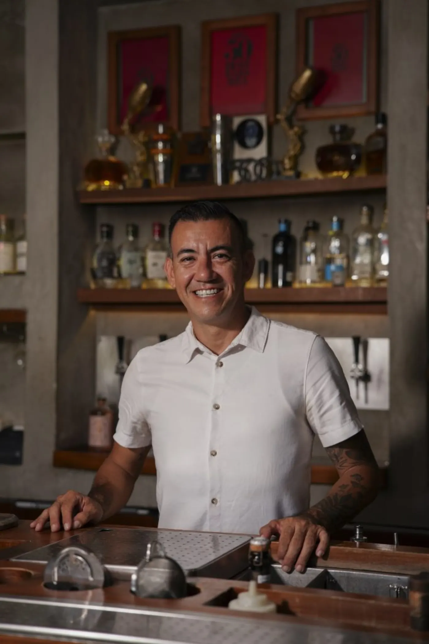Le chef barman du Zapote Bar derrière son comptoir, bouteilles et trophées sur les étagères