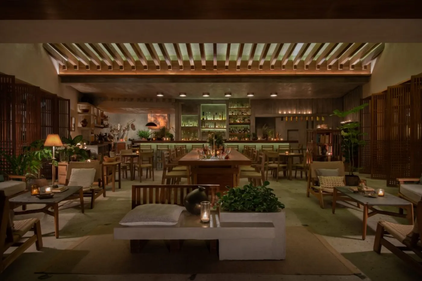 Salle du Zapote Bar le soir : claustras de bois, longue table centrale et bar illuminé au fond