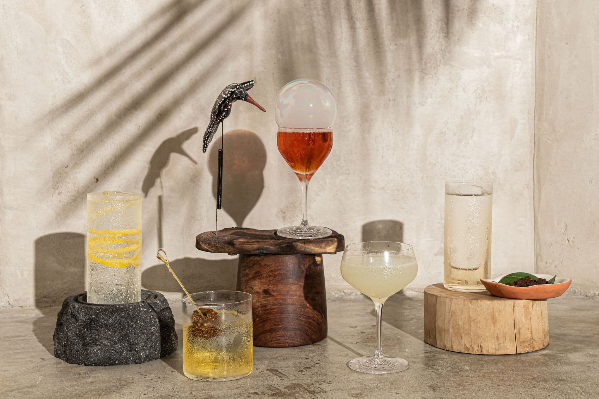 Signature cocktails staged on wood and volcanic stone, one topped with a translucent bubble
