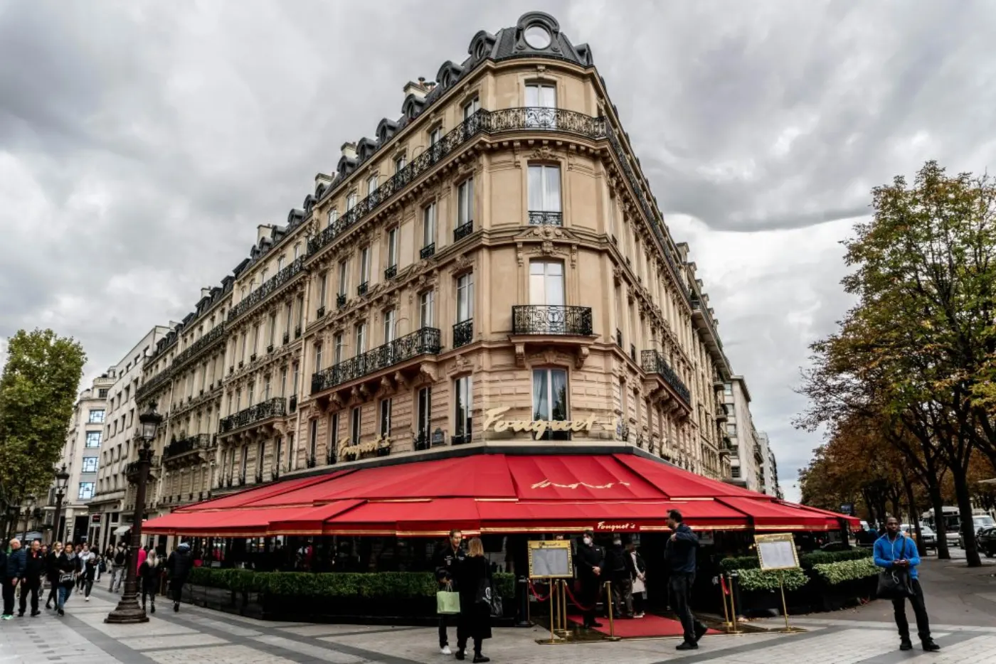 Charming Parisian restaurant with red awnings and classic architecture under a cloudy sky.