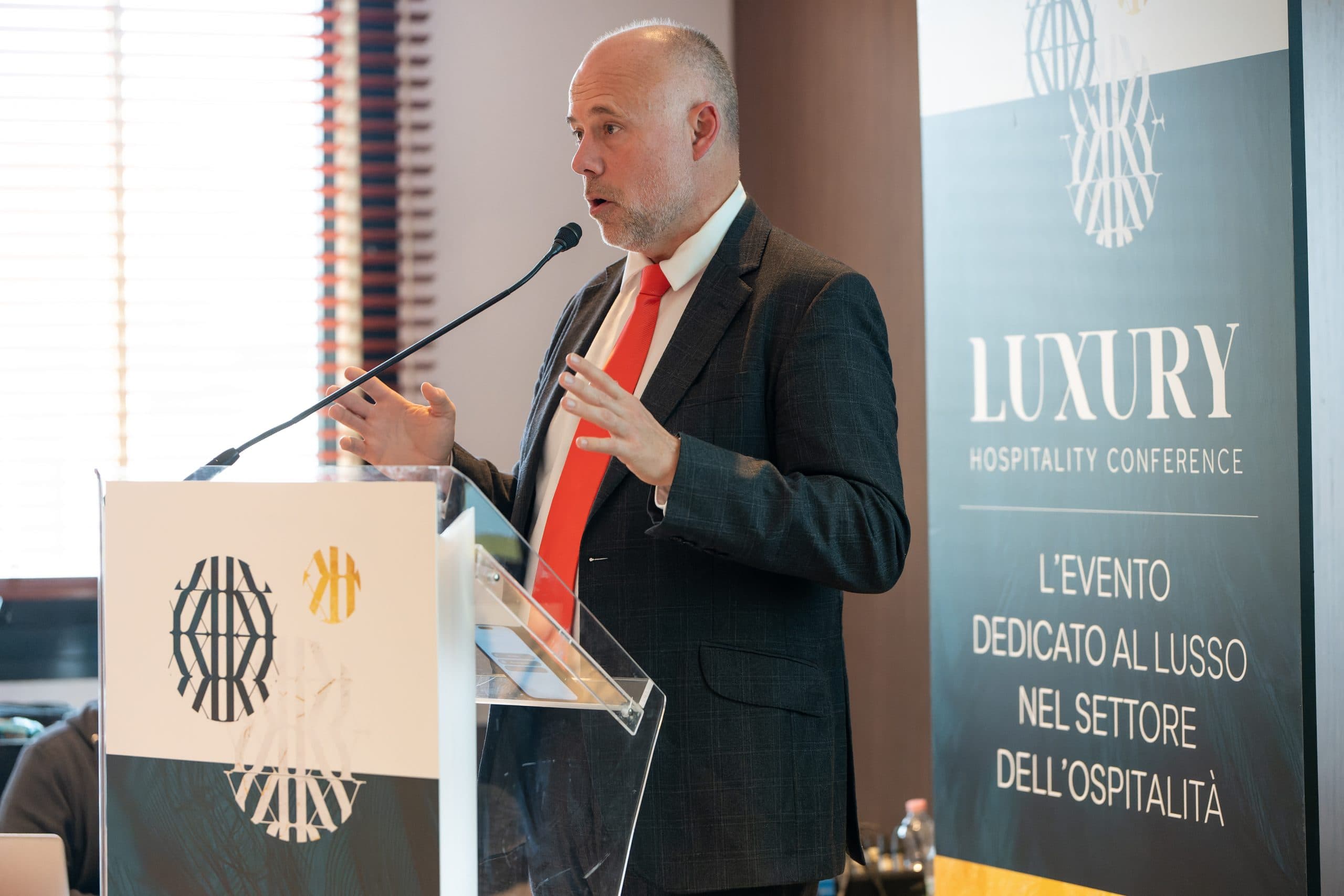 Laurent Delporte au pupitre de la Luxury Hospitality Conference, devant le kakémono de l'événement