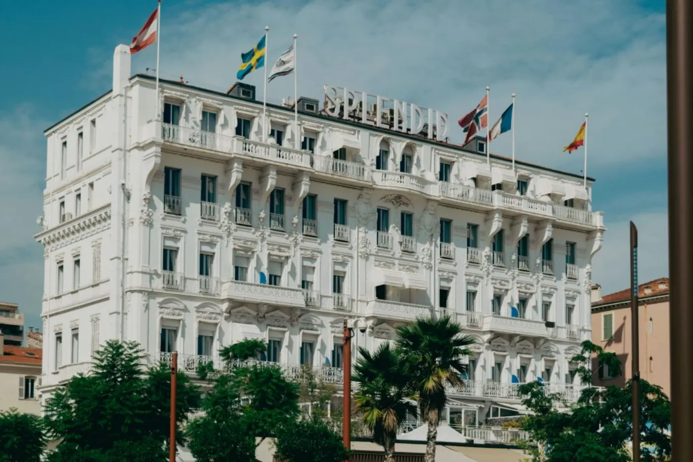 Elegant facade of Hotel Splendid in Cannes with vibrant flags under a sunny sky.