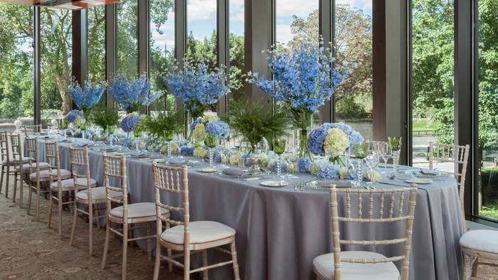 Table de banquet dressée avec de hautes compositions de delphiniums et d'hortensias bleus face au parc
