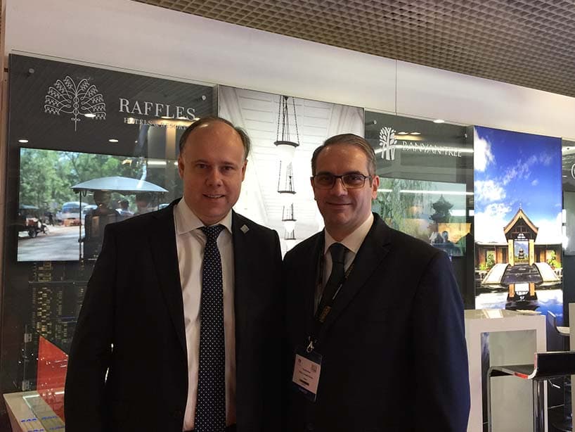 Rencontre sur le stand Raffles et Banyan Tree au salon ILTM, devant les logos des deux marques