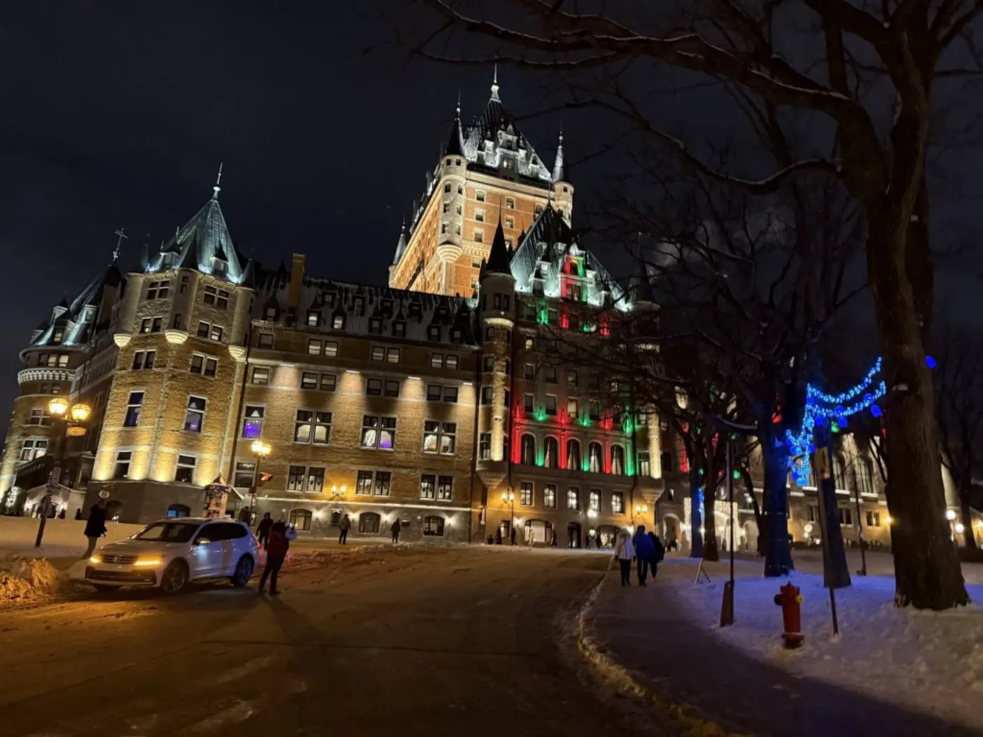 Le Château Frontenac illuminé la nuit sous la neige, façades éclairées de rouge et vert et guirlandes bleues
