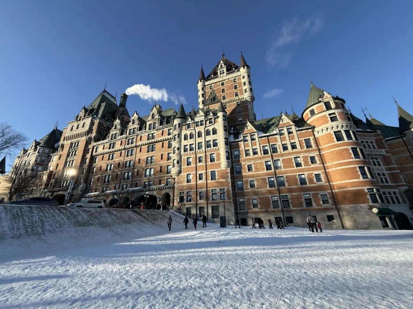 Le Fairmont Le Château Frontenac en contre-plongée par ciel bleu d'hiver, promeneurs sur la terrasse enneigée