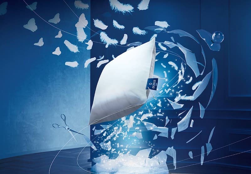 Visuel publicitaire Dumas Paris : oreiller blanc d'où s'échappe une nuée de plumes sur fond bleu