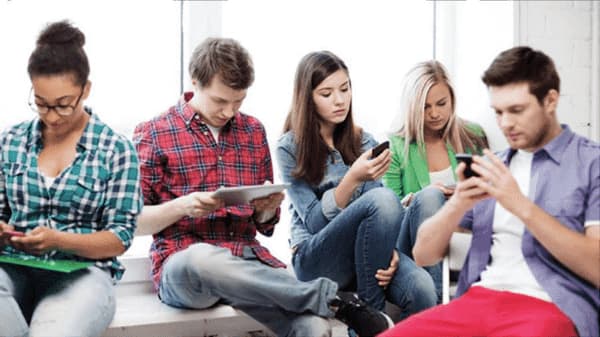 Cinq jeunes assis côte à côte, chacun absorbé par son téléphone ou sa tablette