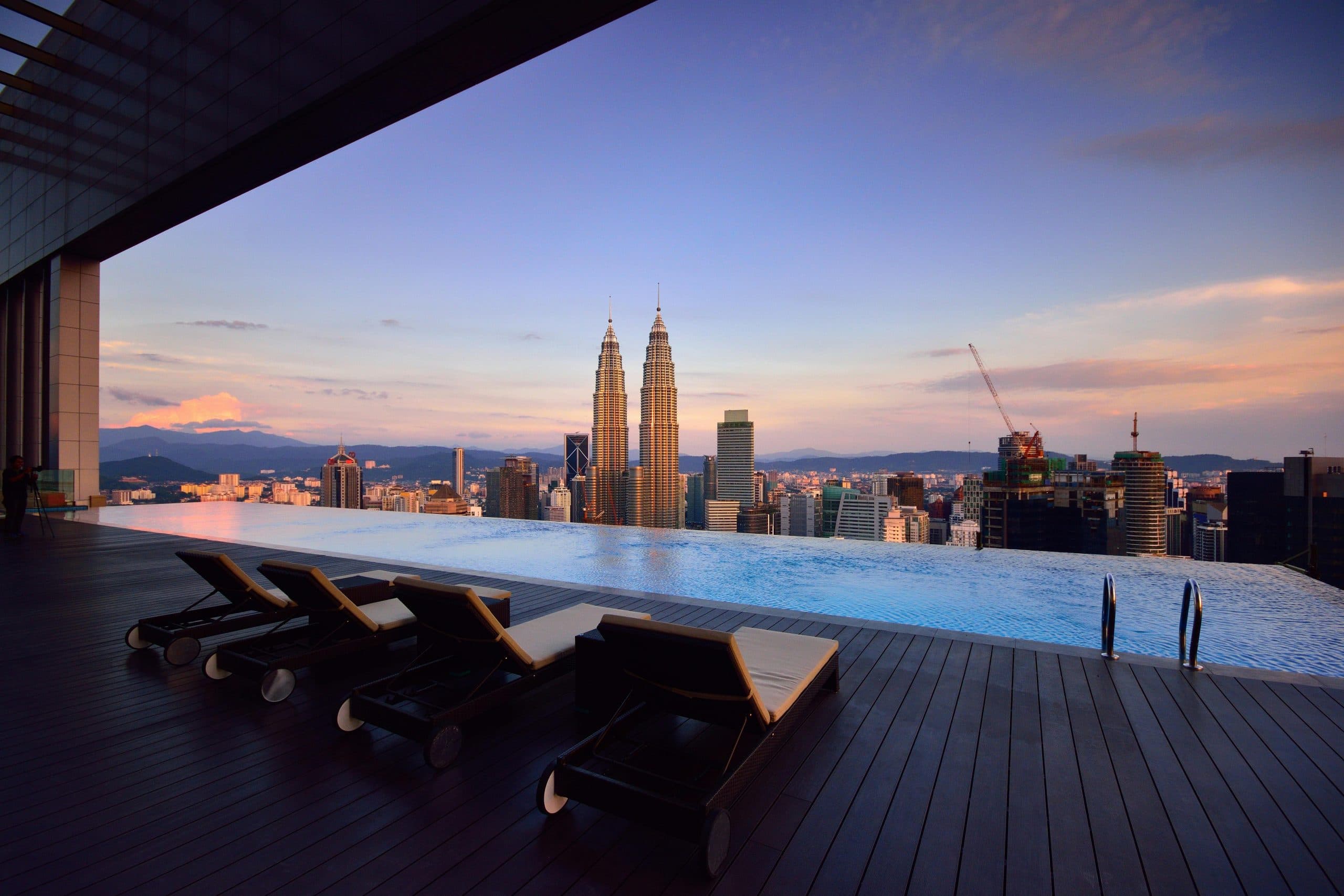 Piscine à débordement en toit-terrasse face aux tours Petronas de Kuala Lumpur au crépuscule