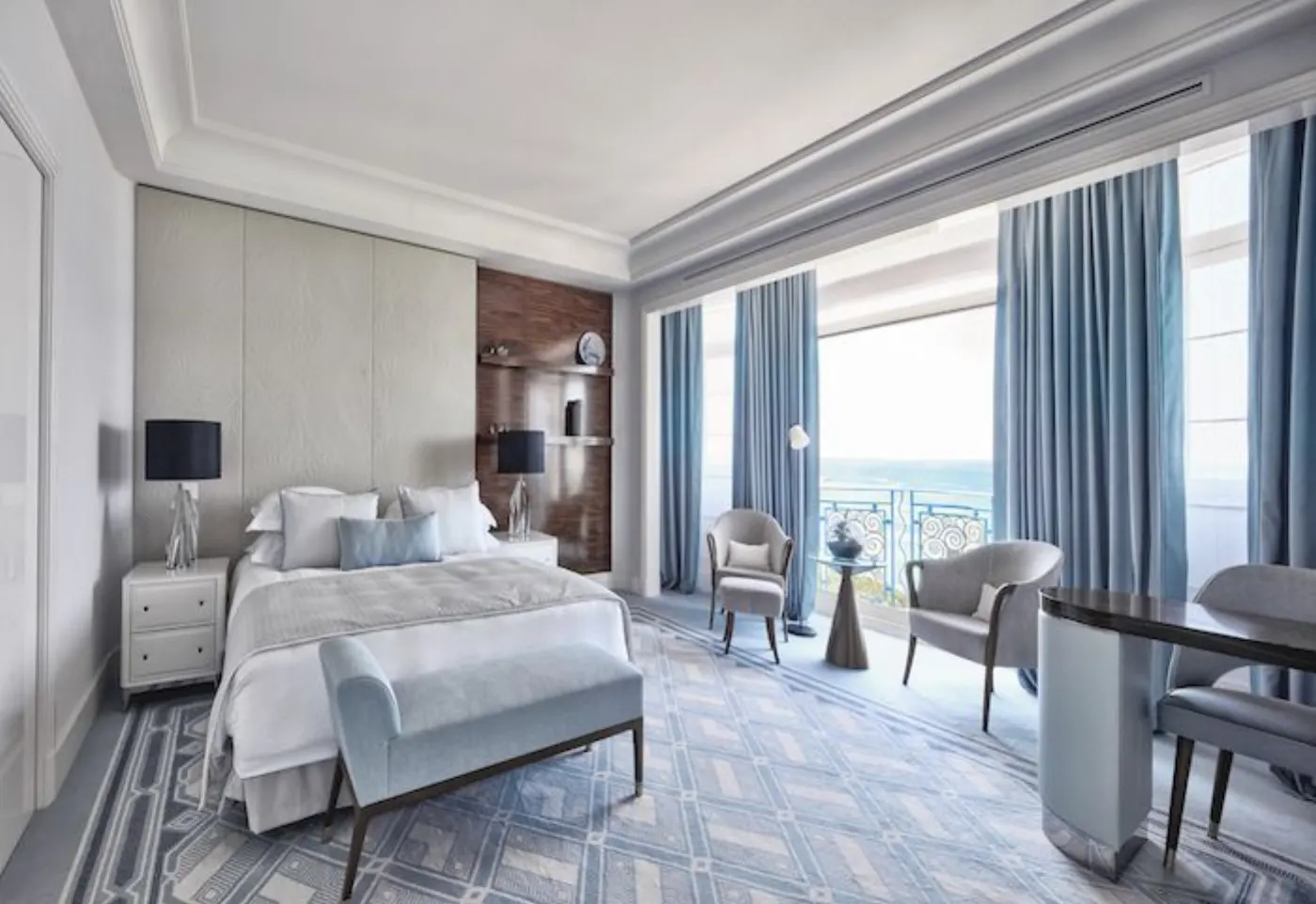 Chambre aux tons bleus face à la mer, rideaux bleu ciel, banquette au pied du lit et fauteuils près du balcon