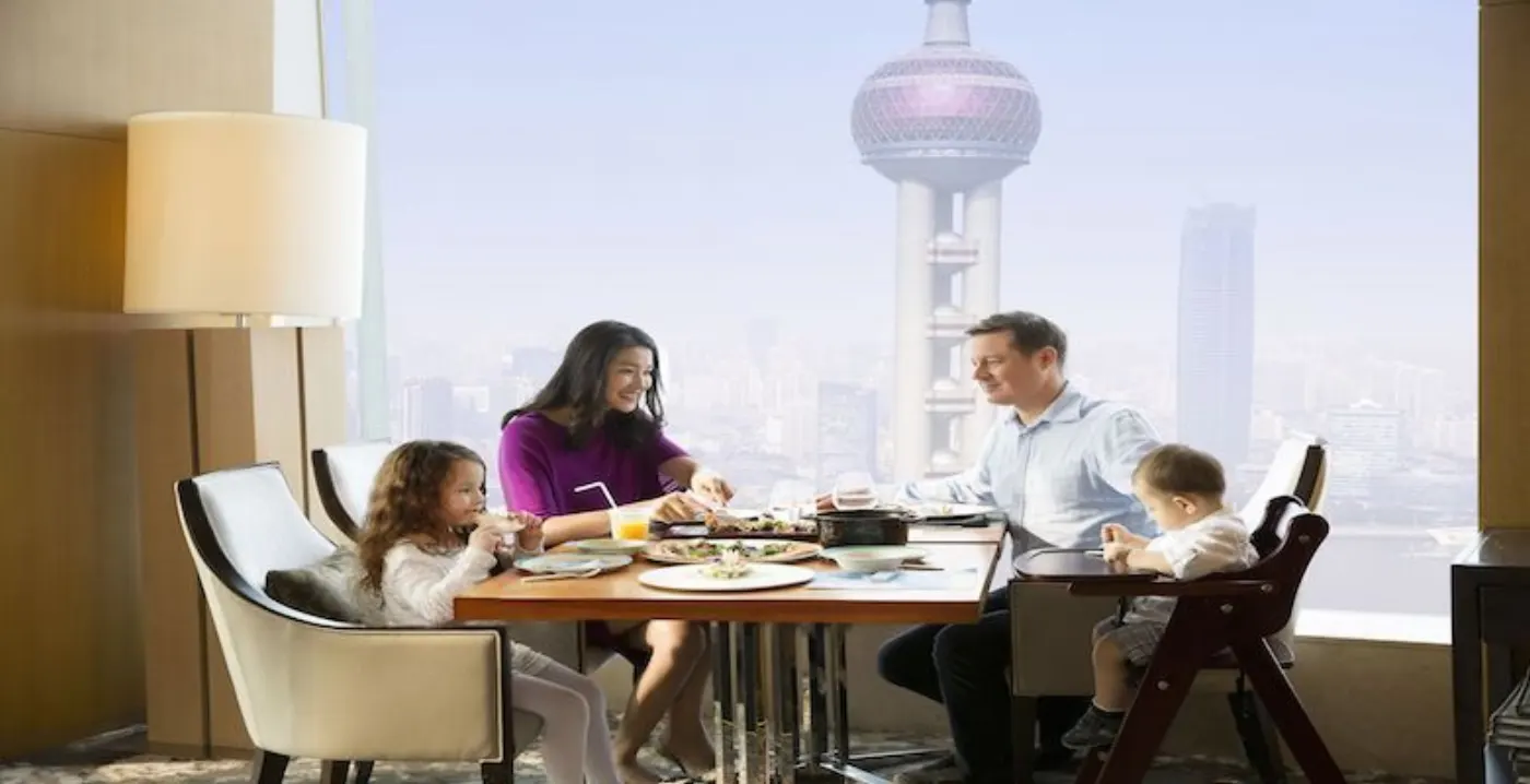 Famille de quatre à table devant la baie vitrée, bébé en chaise haute et Perle de l'Orient en arrière-plan