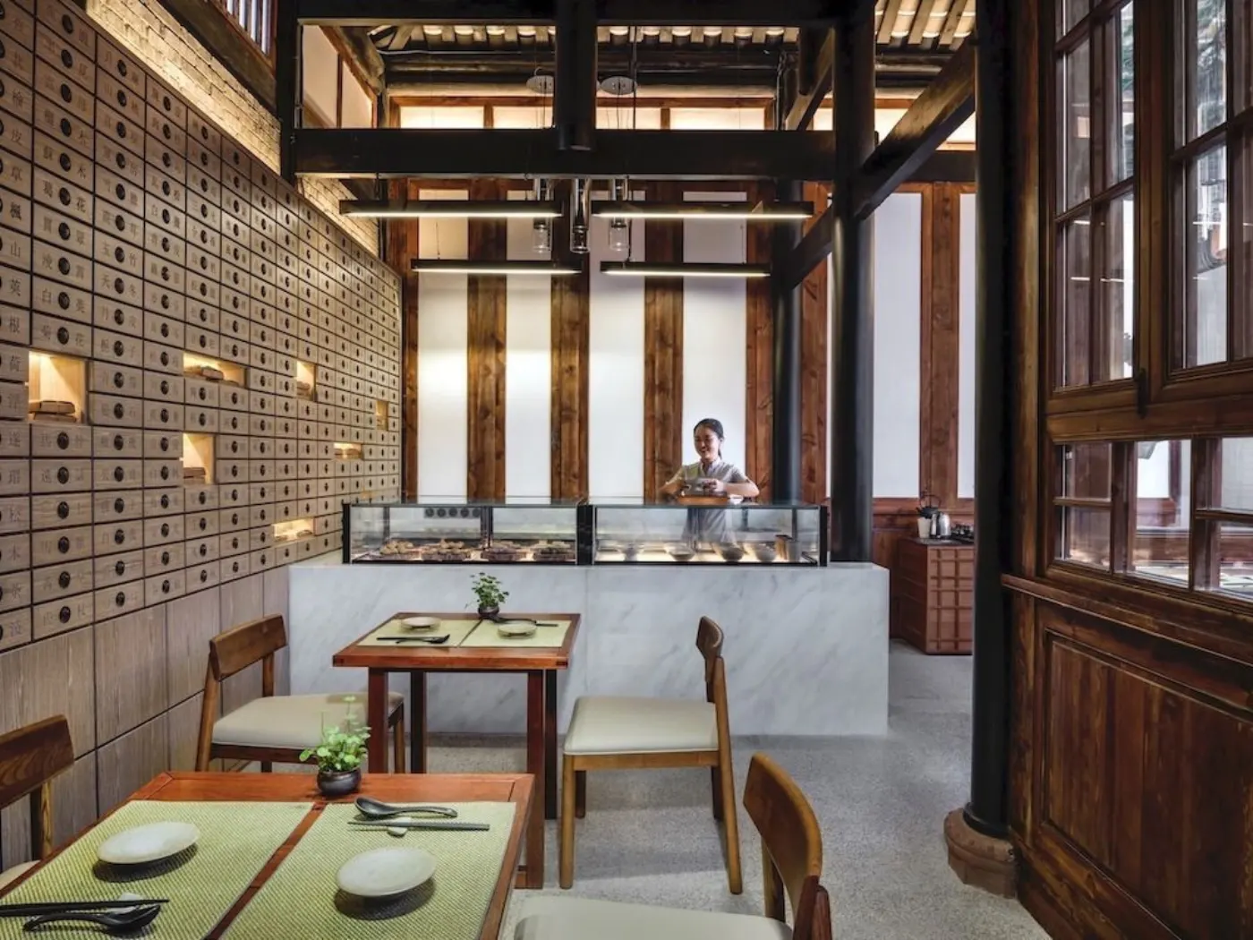 Salle de restaurant dans une maison chinoise en bois : mur de tiroirs d'apothicaire et vitrine de pâtisseries