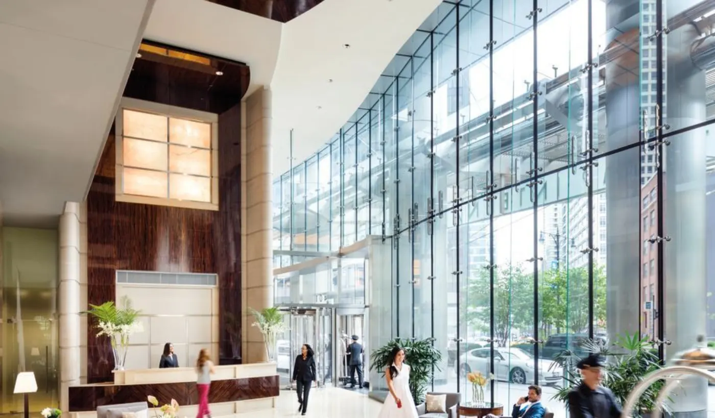 Lobby d'hôtel sous une haute verrière courbe : comptoir de réception, mariée en robe blanche et passants