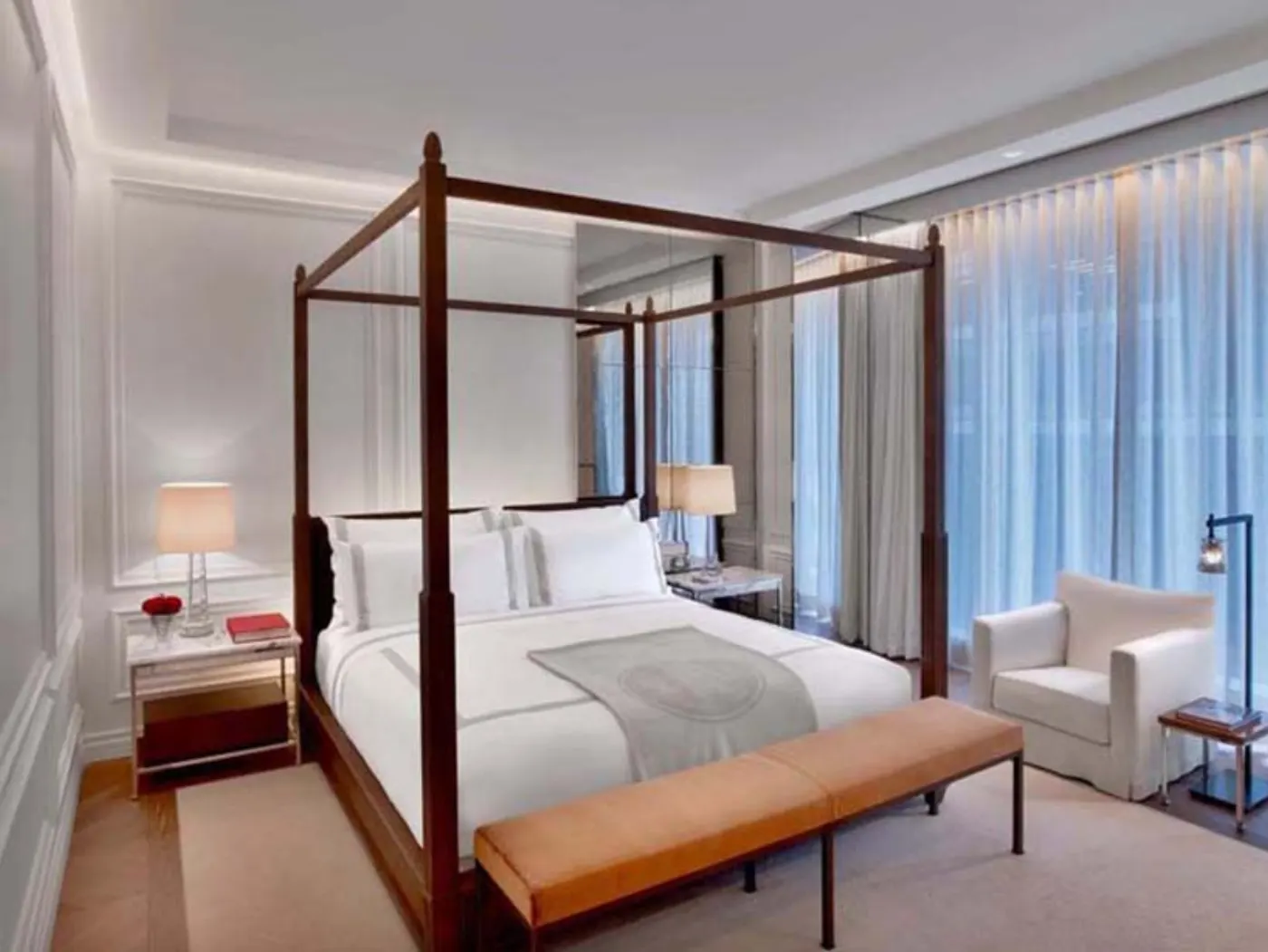Chambre d'hôtel au lit à baldaquin en bois sombre, banquette en cuir orange et rideaux voile clairs