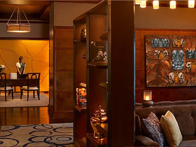 Salon d'un Leela Palace : boiseries chaudes, toile aux tigres et réceptionniste au comptoir en arrière-plan