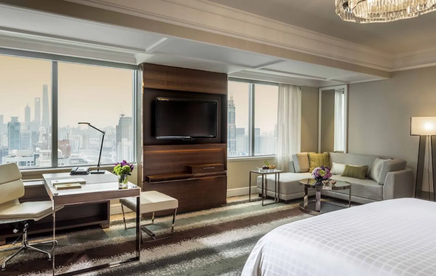 Chambre du Four Seasons Shanghai avec bureau, canapé et baies vitrées ouvertes sur les gratte-ciel de la ville