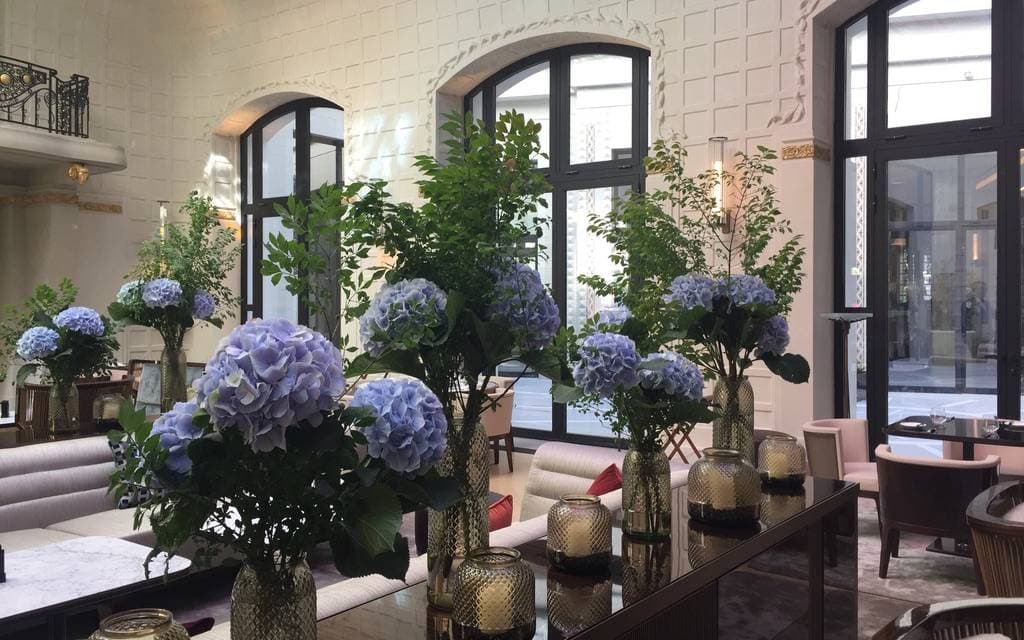 Salon du Lutetia orné de hautes compositions d'hortensias bleus, sous les moulures blanches