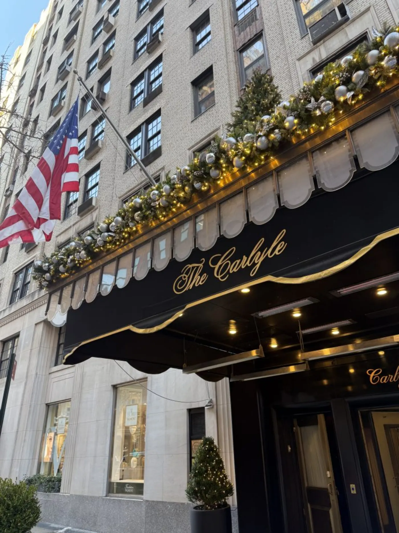 Façade du Carlyle à New York, auvent noir doré, guirlande de Noël argentée et drapeau américain