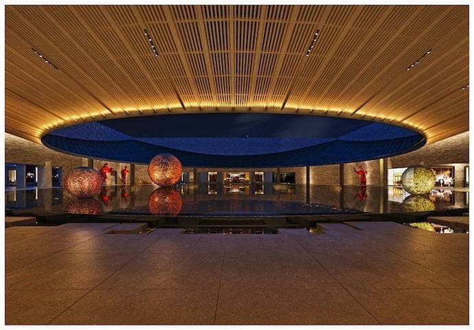 Bassin miroir d'un resort One&Only sous un plafond de bois, sphères lumineuses et danseuses en rouge
