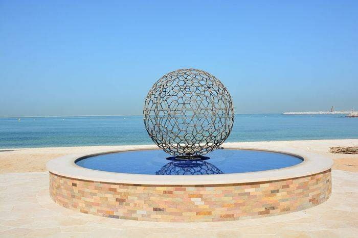 Sphère ajourée posée sur un bassin circulaire, face à la mer turquoise de Dubaï