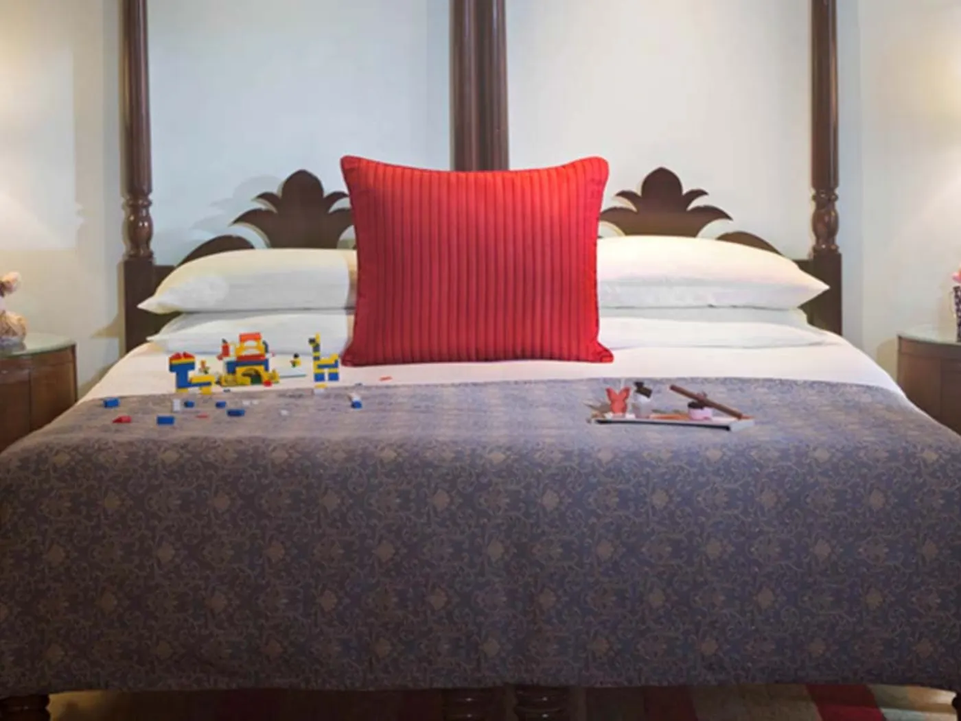 Lit à baldaquin en bois sculpté avec coussin rouge, briques Lego et petits jouets posés sur le couvre-lit