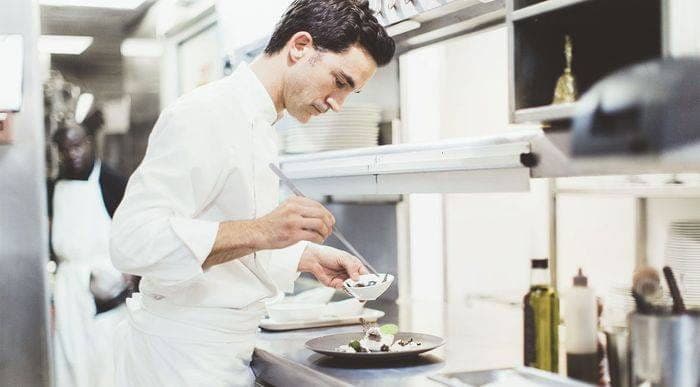 Le chef Patrick Charvet dresse une assiette à la pince, en cuisine, sous la rampe du passe