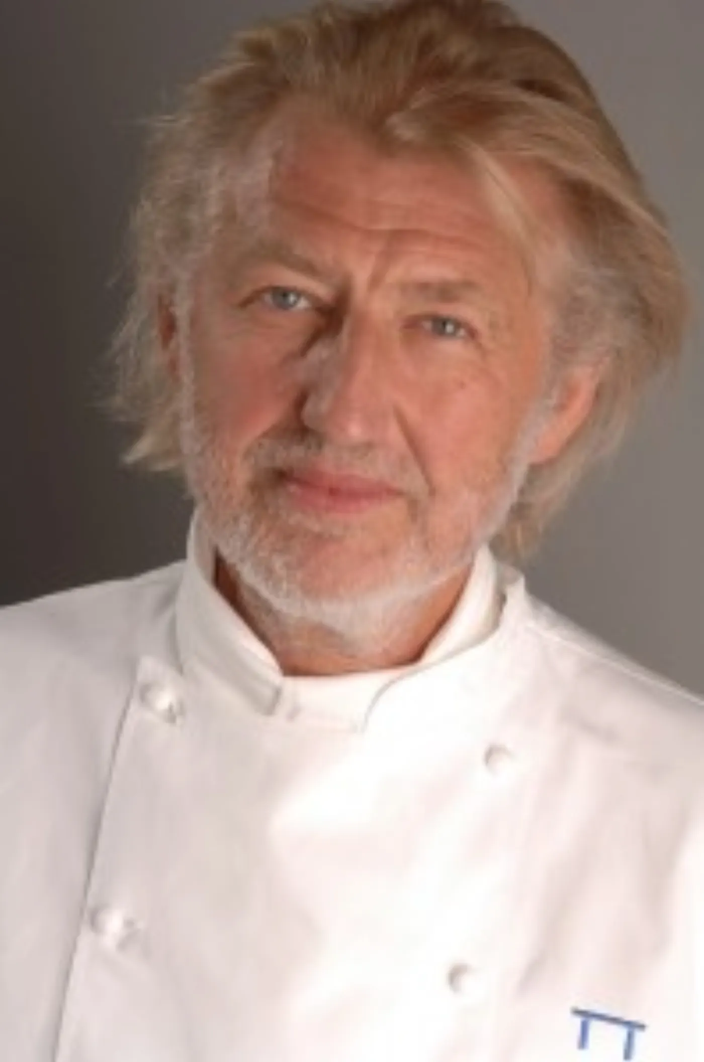 Pierre Gagnaire en veste de cuisinier blanche, cheveux ébouriffés, le regard tourné vers l'objectif