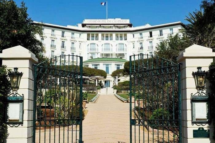 Grille ouverte du Grand-Hôtel du Cap-Ferrat, l'allée menant à la façade blanche et au drapeau