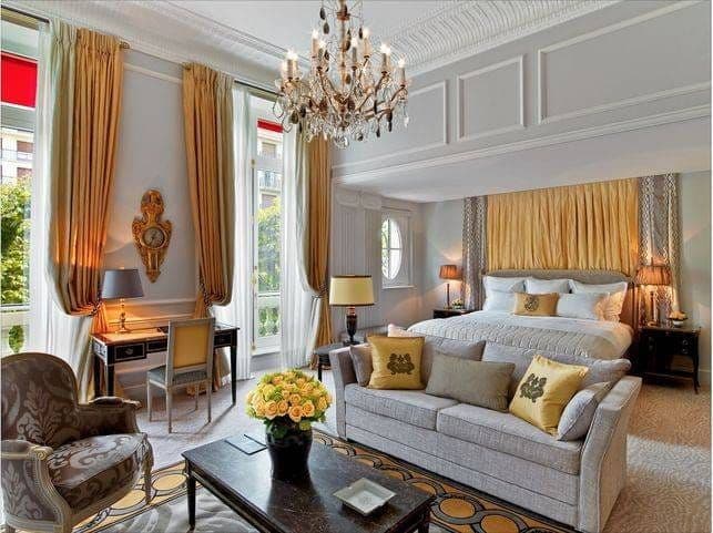 Chambre du Plaza Athénée : lustre de cristal, rideaux et tête de lit dorés, bouquet de roses jaunes
