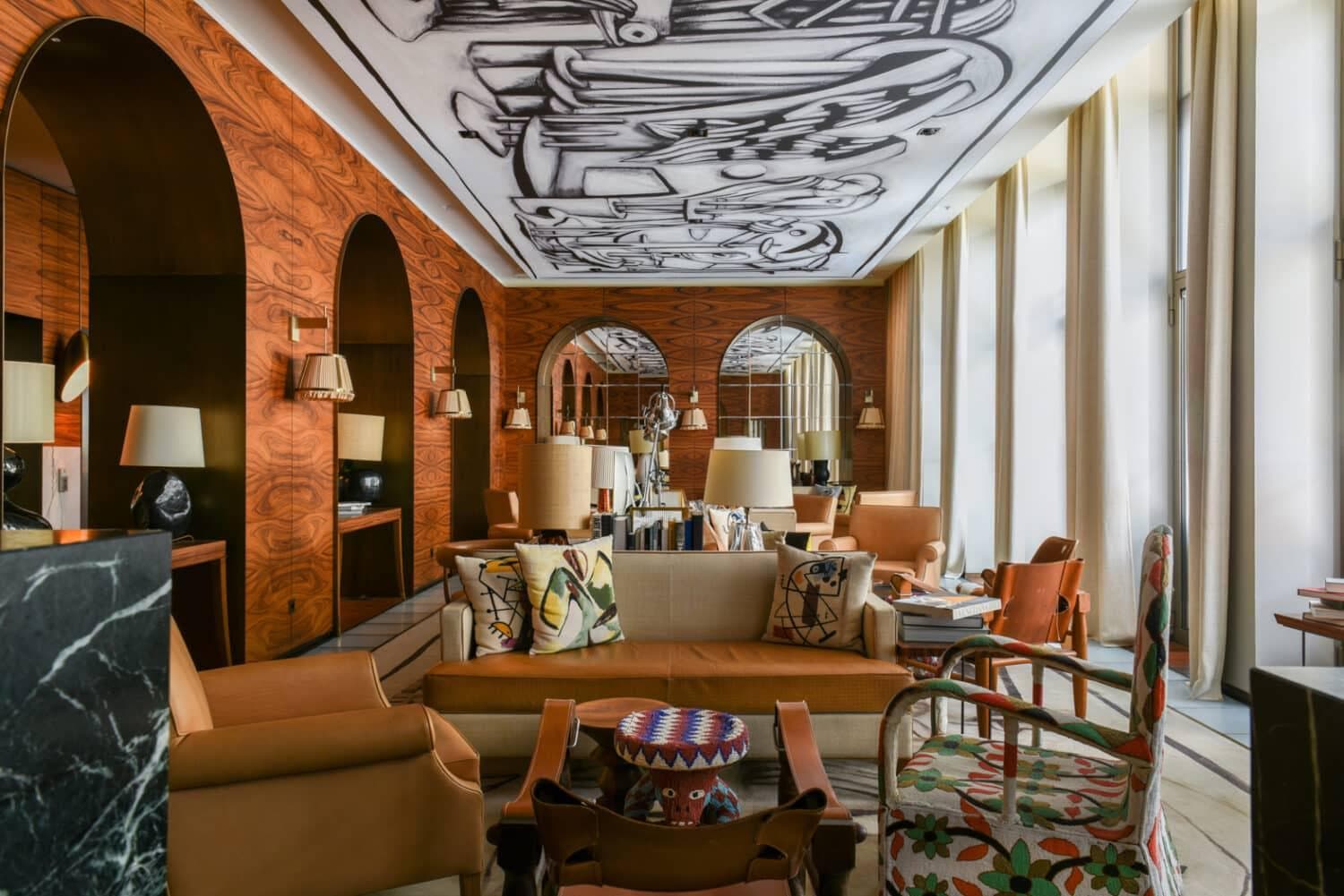 Salon d'hôtel aux arches de bois orangé, plafond dessiné en noir et blanc et fauteuils de cuir fauve
