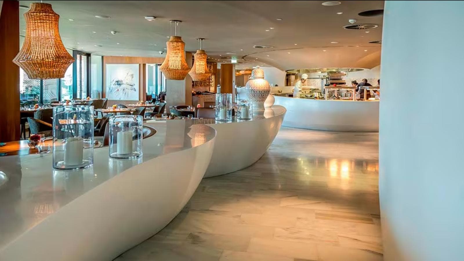Restaurant au comptoir de marbre ondulant, suspensions en osier et cuisine ouverte au fond