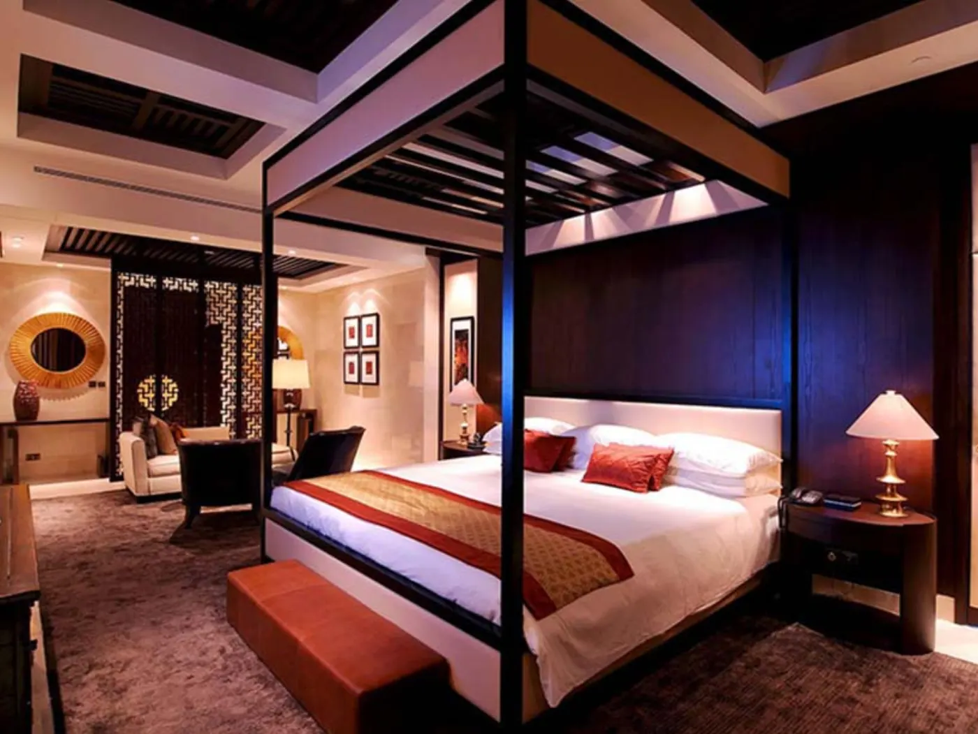 Suite d'hôtel de style asiatique, lit à baldaquin en bois sombre, accents rouges et salon attenant