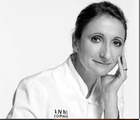 Portrait en noir et blanc de la cheffe Anne-Sophie Pic, en veste blanche, la main contre la joue