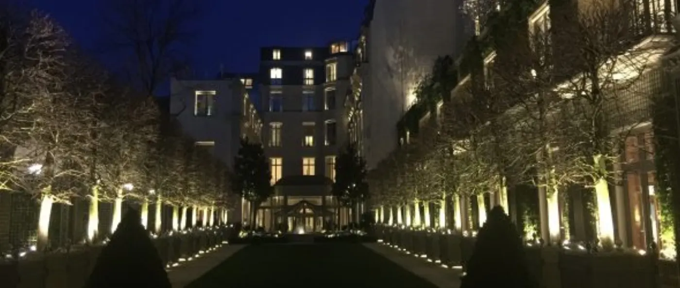 Jardin d'hôtel la nuit, allée bordée d'arbres illuminés menant à la façade éclairée du bâtiment