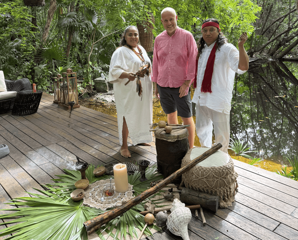 Laurent Delporte flanked by two Mayan healers in white, before a ceremonial altar beside the cenote
