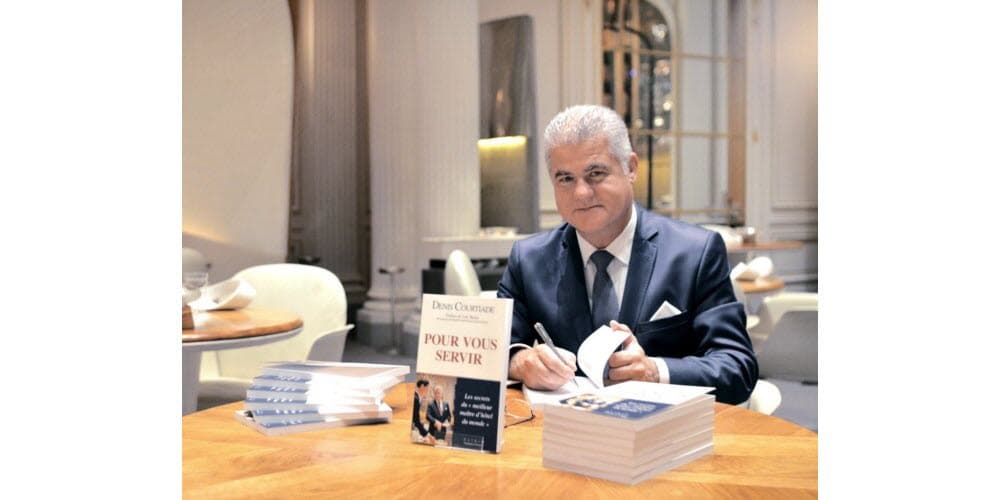Denis Courtiade dédicaçant son livre « Pour vous servir », les exemplaires empilés devant lui