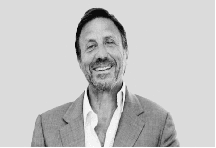 Portrait en noir et blanc de Sir Rocco Forte, souriant, veste claire et chemise ouverte