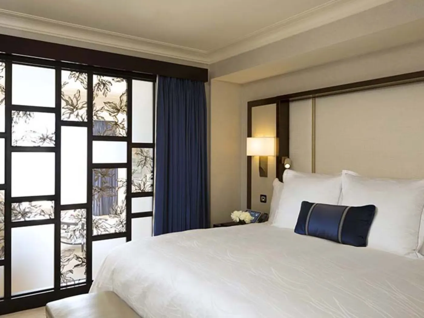 Chambre du Peninsula : literie blanche, traversin bleu marine et cloison laquée noire à motifs floraux