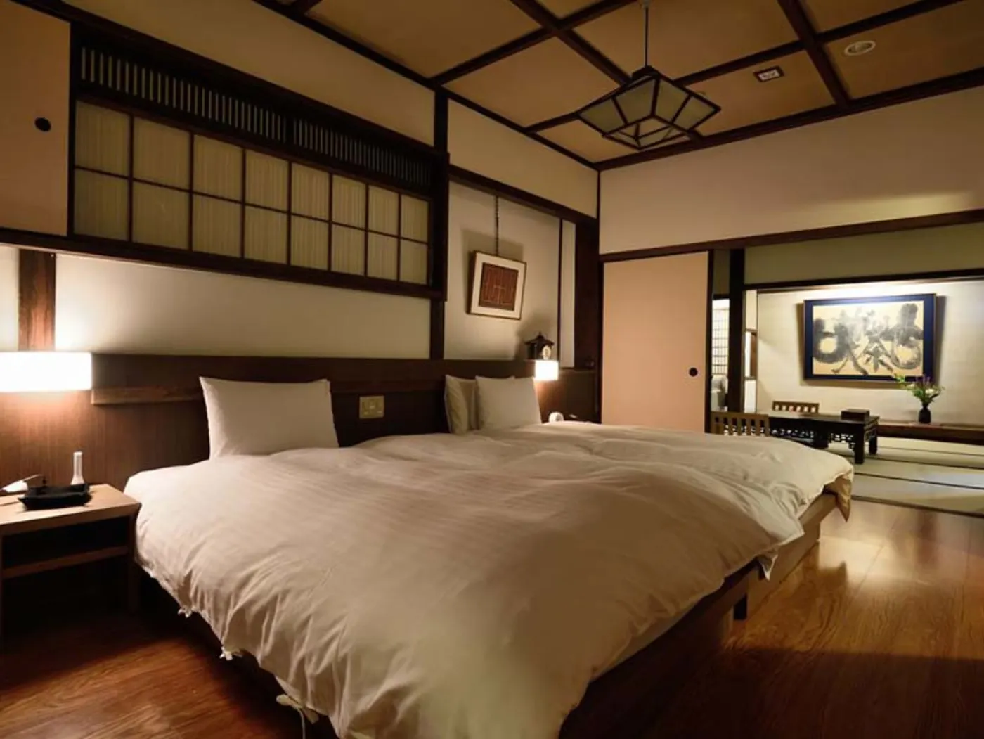 Chambre de ryokan : lit bas et couette blanche, cloisons de bois et shoji, calligraphie au mur